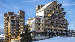 Un hotel de varios pisos con balcones y una pista de esquí al fondo.