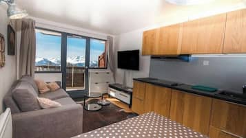 Un espacio habitable compacto con sofá, una mesa de comedor, una zona de cocina con armarios de madera y un televisor.