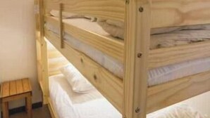 Una cama litera con un taburete de madera cerca, una lámpara de pared y una pared lisa.
