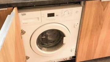 Un lave-linge compact dans une petite cuisine, avec des meubles en bois et un sol carrelé.
