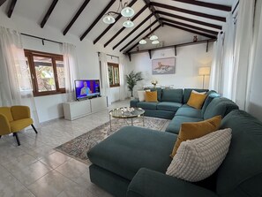 Un salon avec un canapé d’angle, un téléviseur et un fauteuil jaune.