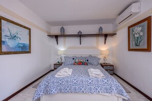 Une chambre à coucher comprenant un lit, deux tables de chevet, une étagère murale décorative et un appareil de climatisation.