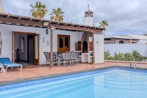 A poolside area with a pergola, outdoor seating, and a view of the surrounding landscape.