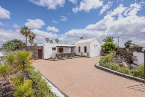A white building with a stone wall, a gravel driveway, and various plants. - 3 Bedroom Villa with Air Conditioning, Parking and Pool (Tías)