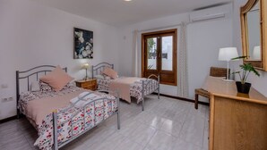 Une chambre avec deux lits, un bureau en bois, une chaise, une plante en pot et une fenêtre avec des rideaux.