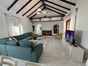 Una sala de estar con un sofá seccional, una chimenea, un televisor y un comedor.