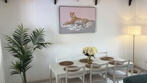 Un coin repas avec une table blanche, des sets de table en fibres tressées et des chaises. Un tableau encadré représentant un léopard est accroché au mur.