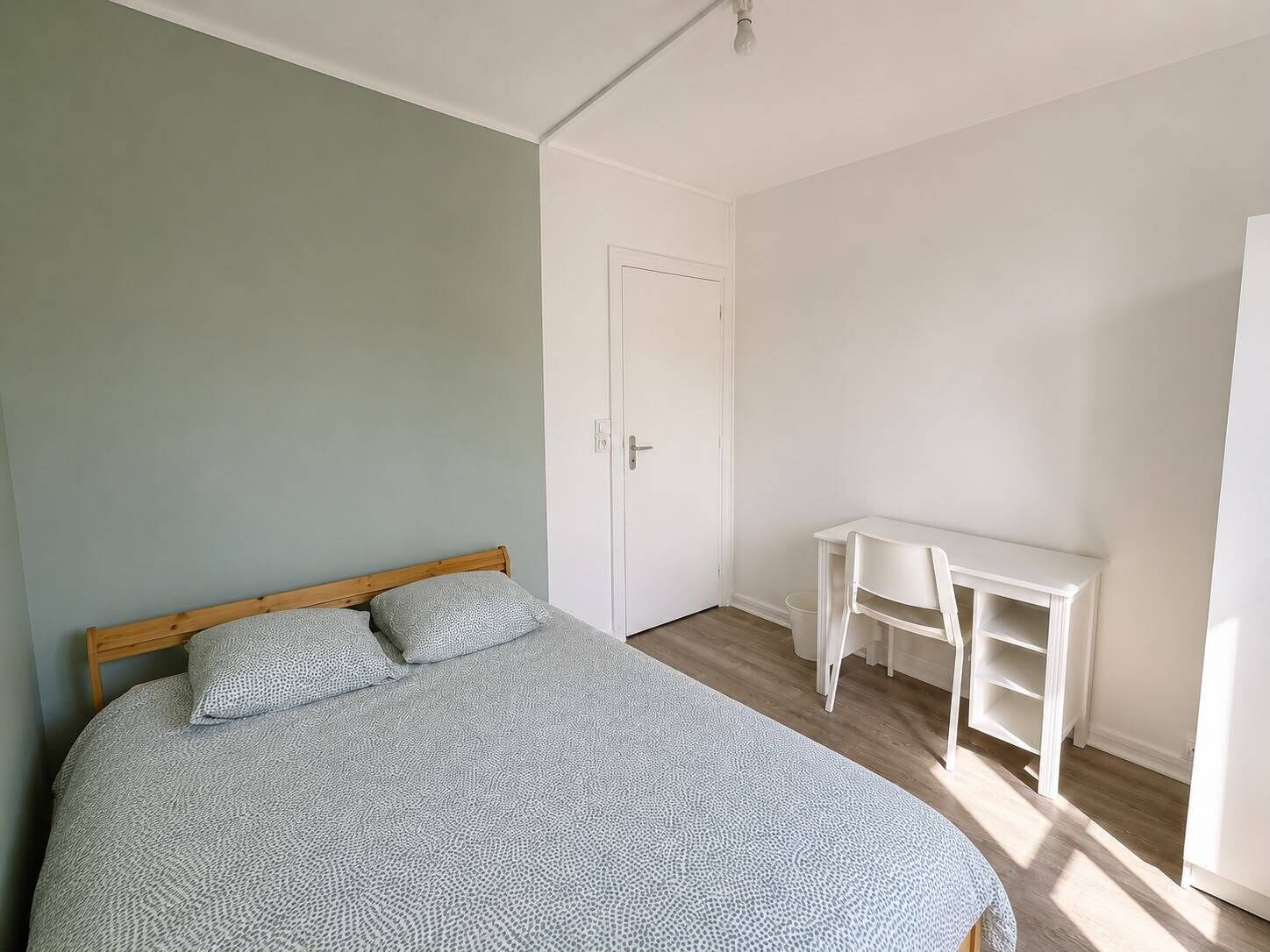 Un dormitorio con cama, escritorio y puerta.