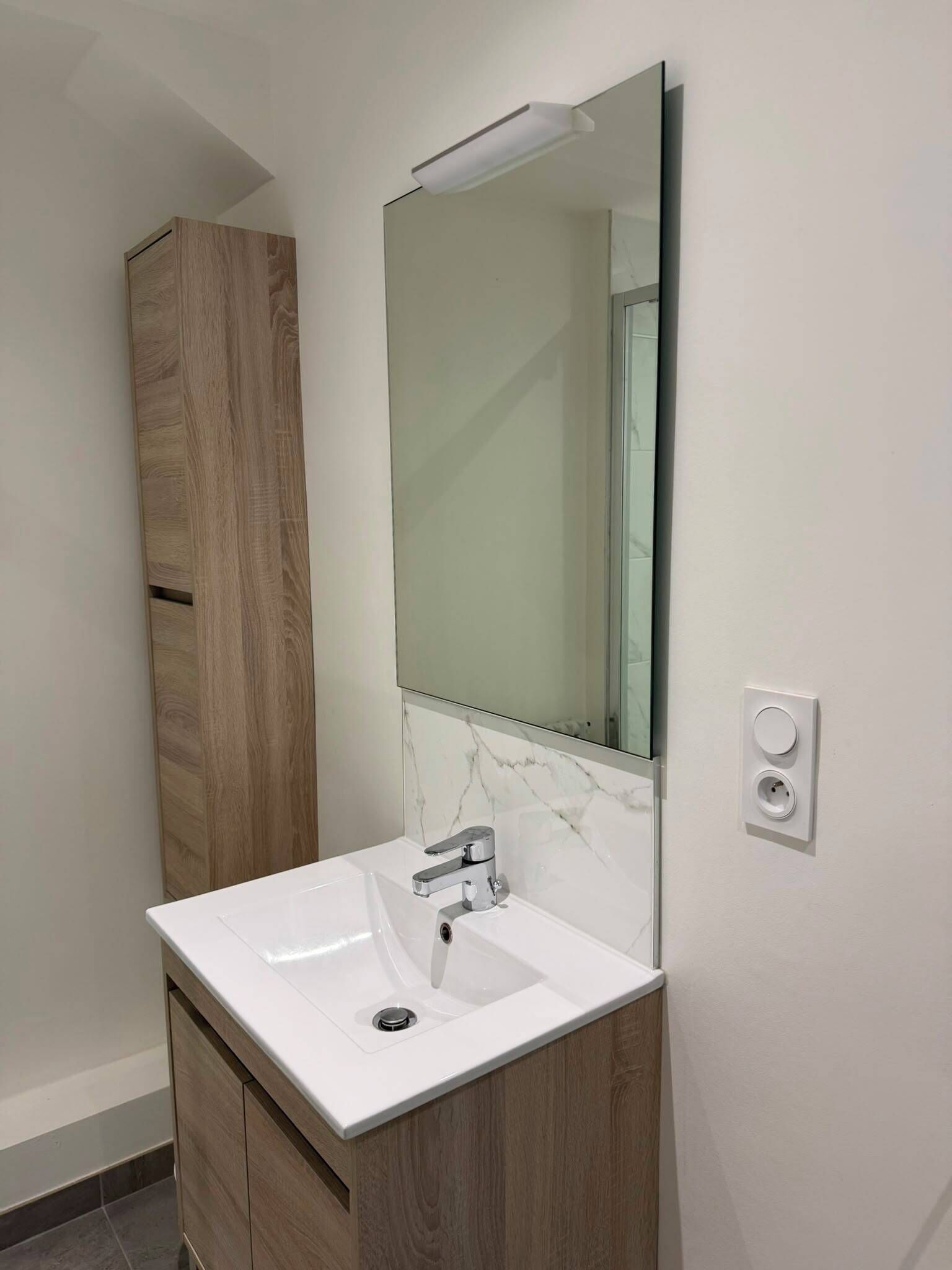 A bathroom with a white sink, a wooden cabinet, and a mirror.