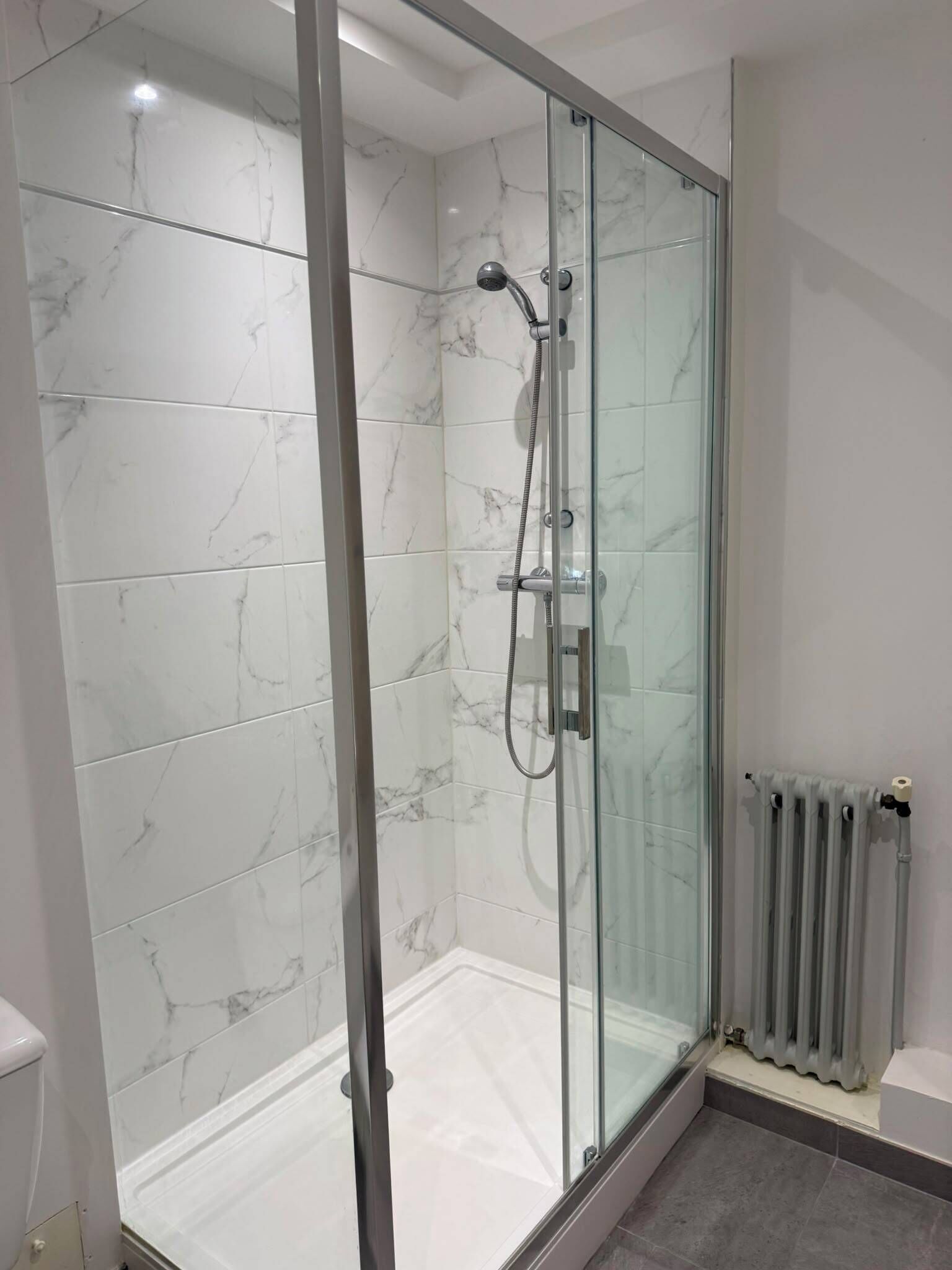 A modern bathroom with a glass-enclosed shower, marble tiles, and a visible toilet.