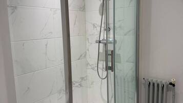 A modern bathroom with a glass-enclosed shower, marble tiles, and a visible toilet.