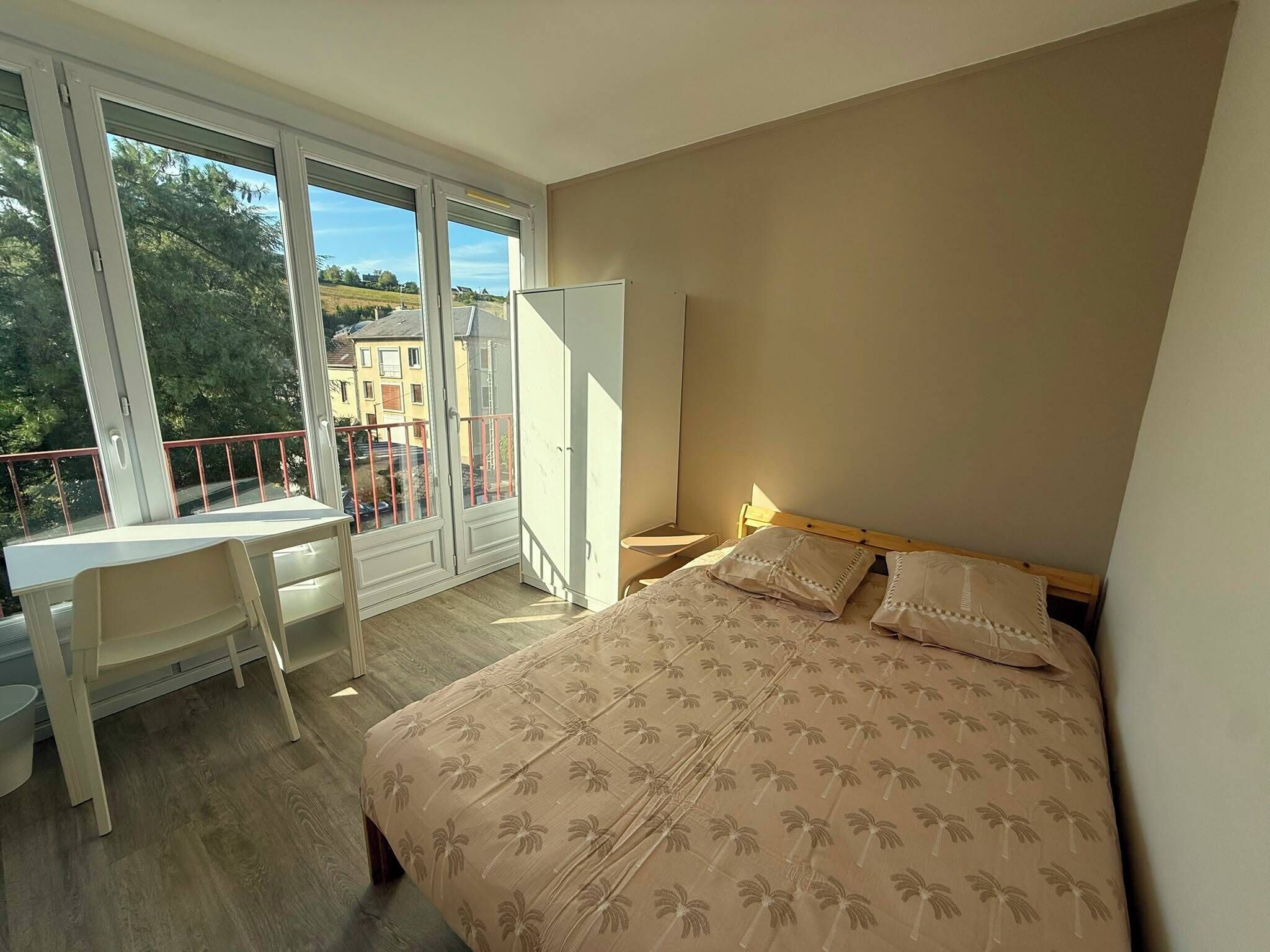 A bedroom with a bed, a desk, and a balcony.