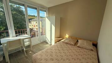 A bedroom with a bed, a desk, and a balcony.