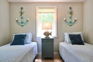A bedroom with two beds, a window with a lamp, and decorative anchors on the walls. - Raynor Shine | Walk to Beach | Family Fun | Dog Friendly (Falmouth)