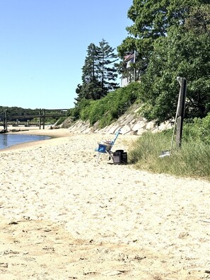 Une plage de sable avec une chaise bleue et un sac, un poteau en bois et un pont en arrière-plan.