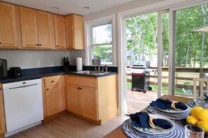 A kitchen with wooden cabinets, a dishwasher, a sink, and a view of the outdoors. - Raynor Shine | Walk to Beach | Family Fun | Dog Friendly (Falmouth)