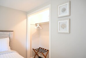 Une chambre à coucher avec un lit, un étendoir en bois, une armoire avec un cintre et deux tableaux encadrés au mur.