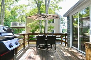 A wooden deck with a grill, two chairs, and an umbrella. - Raynor Shine | Walk to Beach | Family Fun | Dog Friendly (Falmouth)