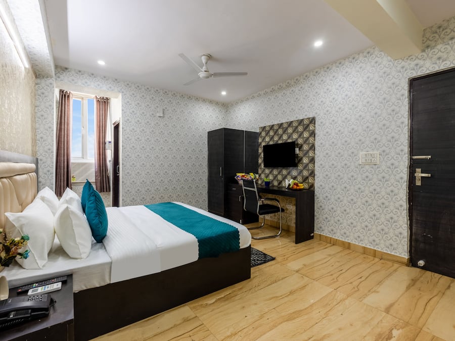 A bedroom with a bed, desk, chair, TV, and a door.