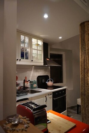 A compact kitchen with white cabinets, a black stove, and a red chair. - Traverse du Vieux Château (Menton)