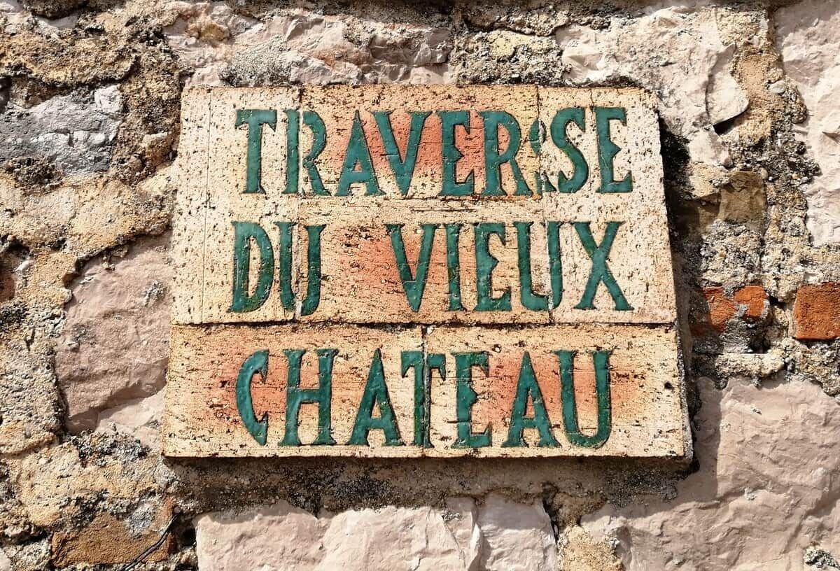 Ein Schild mit dem Text 'TRAVERSE DU VIEUX CHATEAU' an einer Ziegelwand.