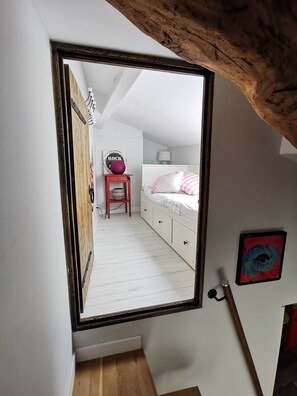 A bedroom with a white bed, a bedside table with a lamp, and a wall-mounted mirror. - Traverse du Vieux Château (Menton)