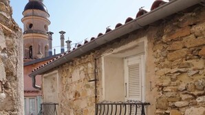 A narrow street with stone buildings, a bell tower, and a small balcony with a metal railing. - Traverse du Vieux Château (Menton)