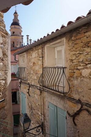 A narrow street with stone buildings, a bell tower, and a small balcony with a metal railing. - Traverse du Vieux Château (Menton)