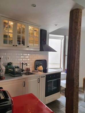 A kitchen with white cabinets, a black stove, and a window with a view. - Traverse du Vieux Château (Menton)