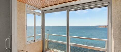 A balcony with a view of the sea, a wicker chair, and a table with cups.
