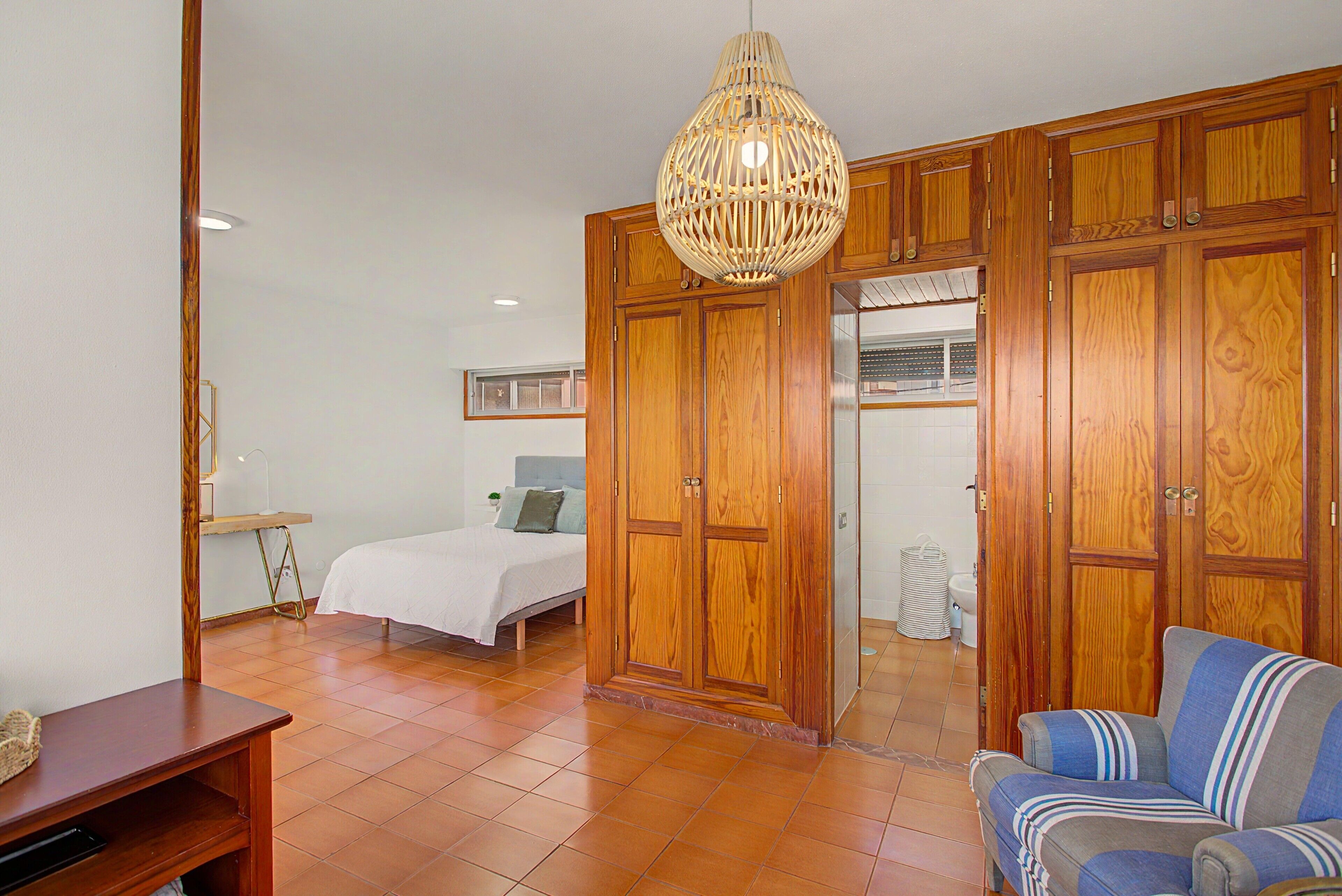 Une chambre à coucher comprenant un lit, une armoire en bois, un luminaire suspendu et un canapé.