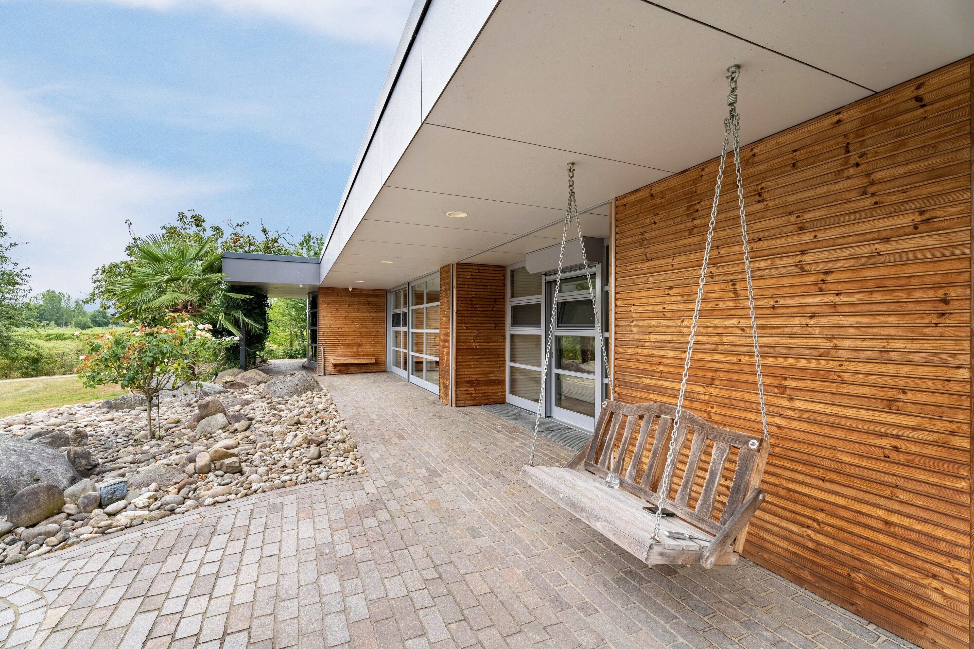 A modern building exterior with a wooden facade, a stone pathway, and a wooden swing.