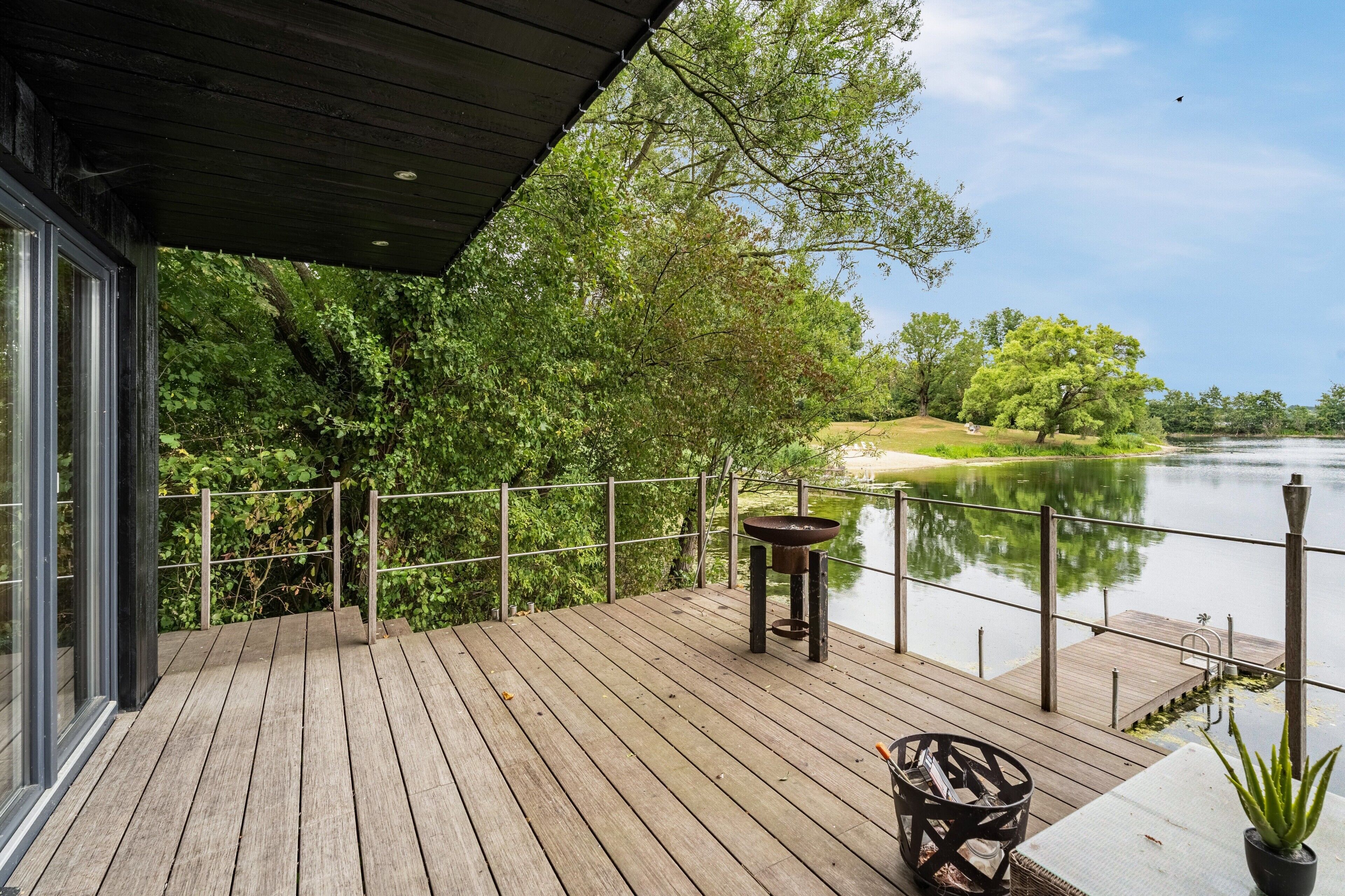 Une terrasse en bois offrant une vue sur une rivière paisible, entourée d’arbres.