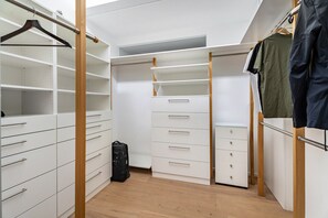 A walk-in closet with multiple drawers and shelves, a hanging rod, and a suitcase on the floor.
