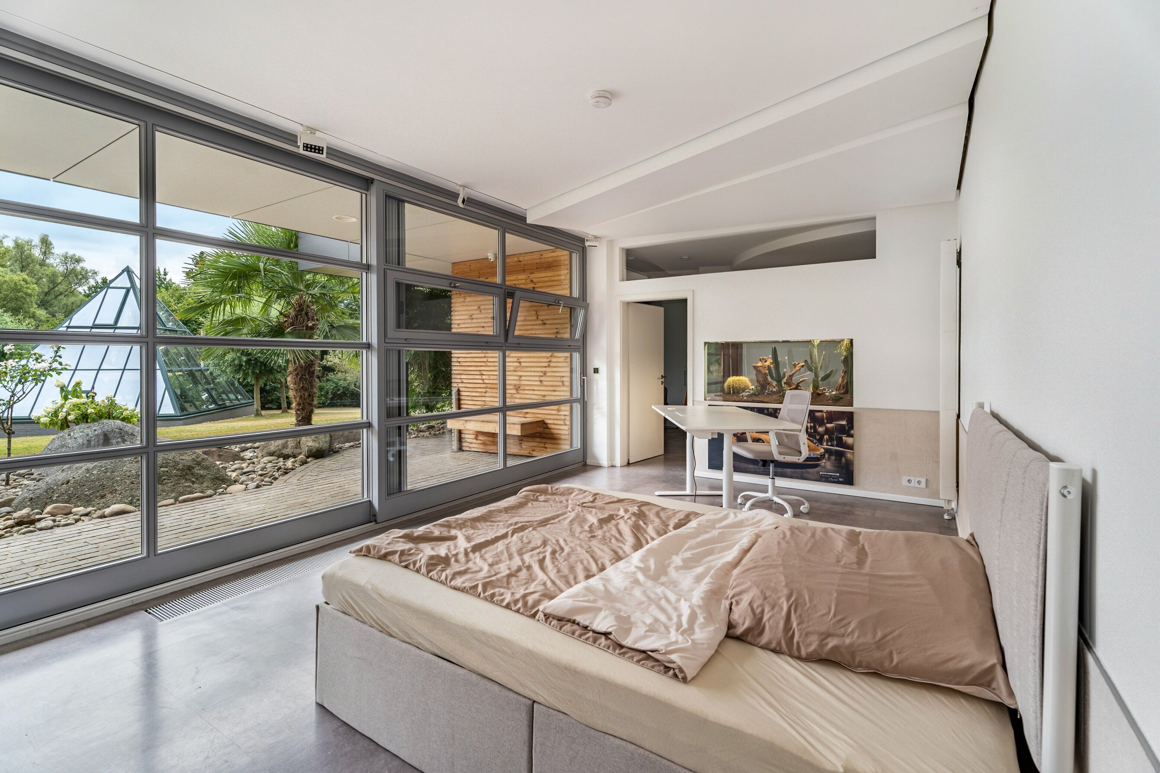 A modern bedroom with a large sliding glass door, a bed, a desk, and a chair.