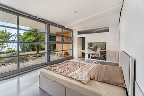 A modern bedroom with a large sliding glass door, a bed, a desk, and a chair.