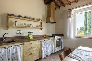 A kitchen with wooden shelves, a stove, and a window with a view of trees.