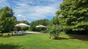 Un cortile con piscina, due ombrelloni e un prato.