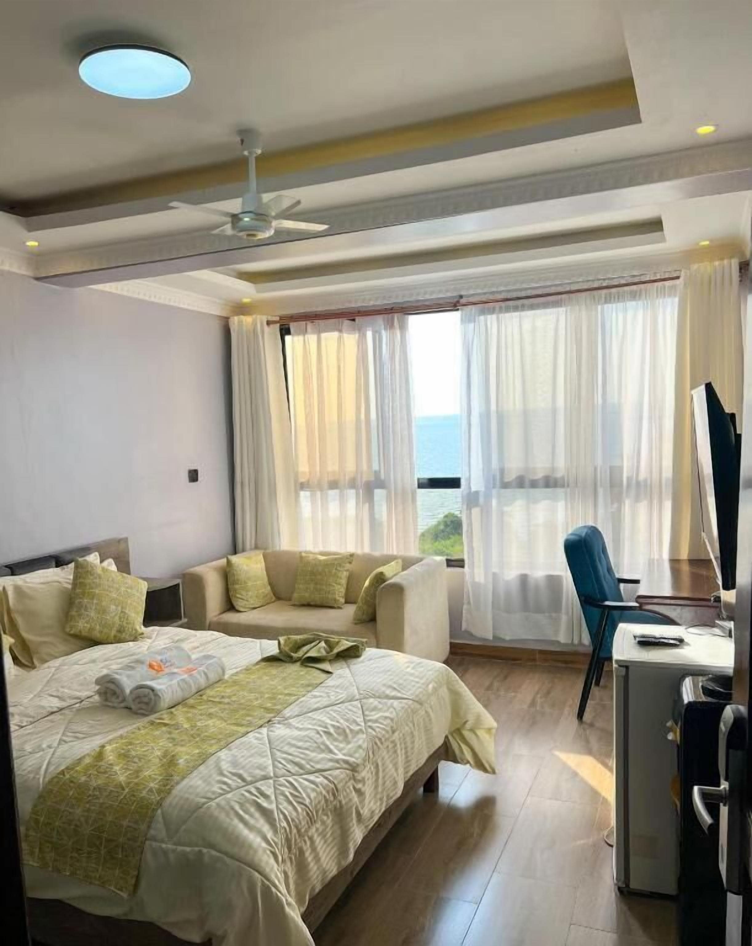 A hotel room with a bed, a desk, and a chair. There is a window with curtains.