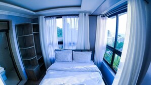 Ein Schlafzimmer mit einem Bett, einem Vorhangfenster, einer eingebauten Ablagefläche und Blick ins Freie.