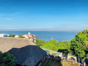 A coastal view with buildings, a thatched-roof structure, and lush greenery.