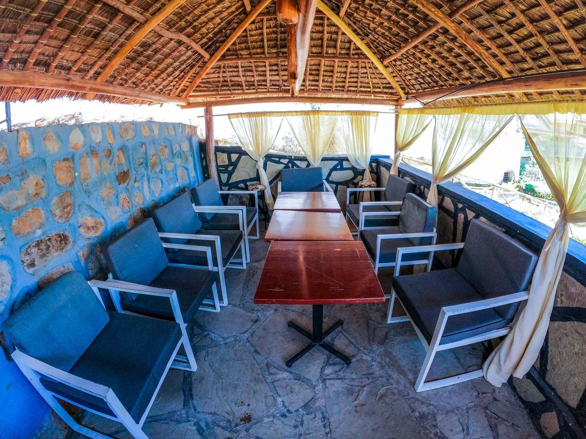 An outdoor seating area with a thatched roof, stone walls, and blue cushioned chairs.