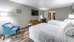 Habitación de hotel con dos camas, un escritorio, una silla, un televisor y una puerta que da a otra habitación.