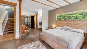 A bedroom with a large bed, wooden beams, a view of greenery, and a staircase. - Stellar Peak Chalet 3 Bedroom Home (Montezuma)