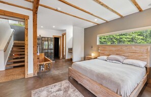 Ein Schlafzimmer mit einem großen Bett, Holzbalken, Blick ins Grüne und einer Treppe.