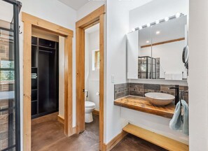 Ein modernes Badezimmer mit einem Holz-Waschtisch, einem großen Spiegel und einer integrierten Dusche.