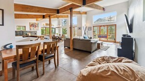 A spacious living area with a dining table, chairs, a sofa, and a large window with a view of trees. - Stellar Peak Chalet 3 Bedroom Home (Montezuma)