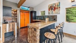 A modern kitchen with a wooden island, bar stools, and a cityscape painting. - Stellar Peak Chalet 3 Bedroom Home (Montezuma)