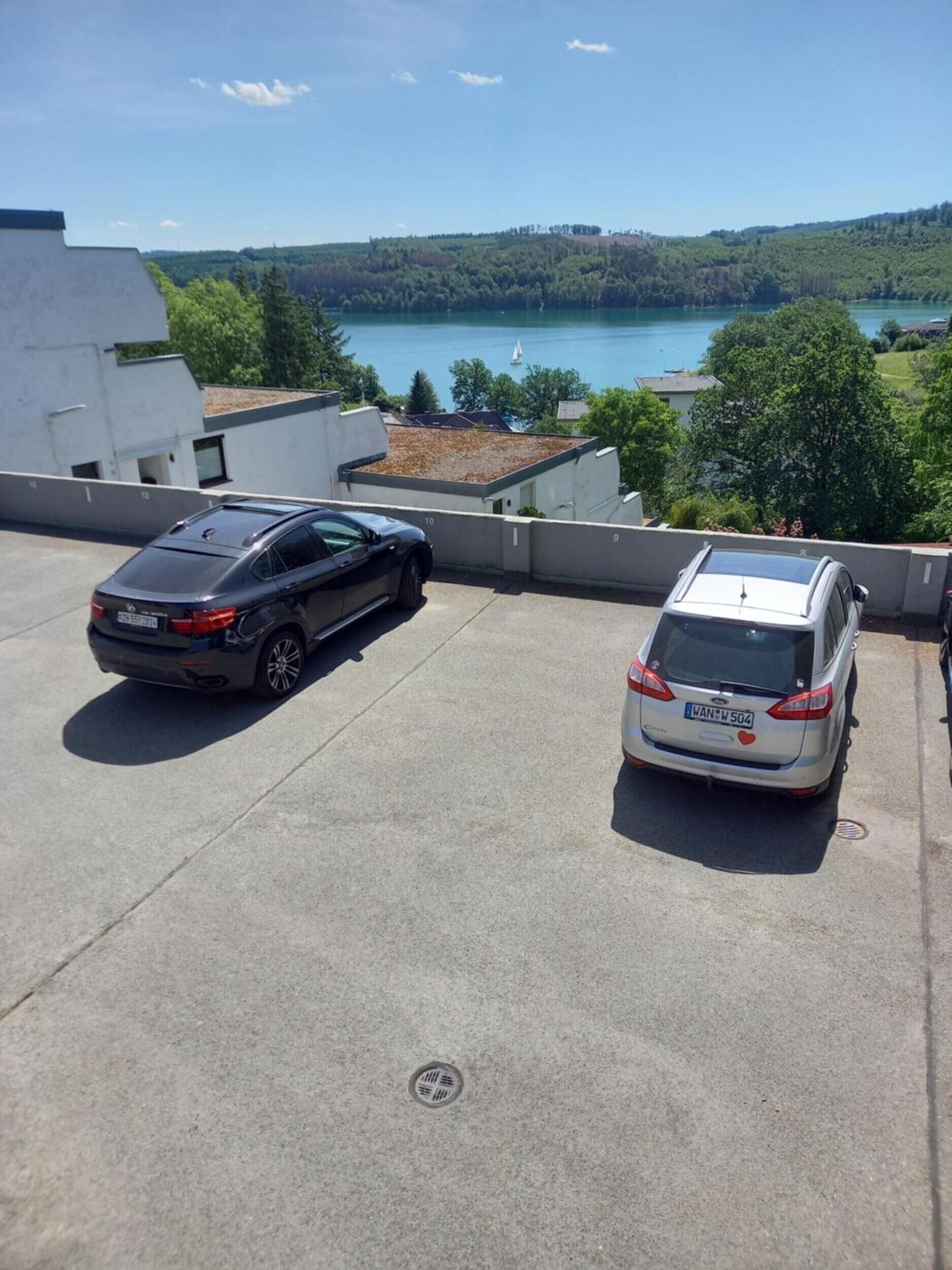 Two cars parked on a rooftop with a view of a lake and hills.