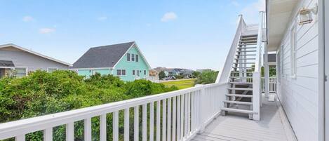 A wooden deck with a white railing, a staircase leading to a porch, and a turquoise house in the background.